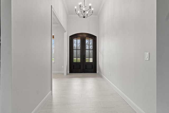 foyer featuring arched walkways, baseboards, french doors, ornamental molding, and an inviting chandelier