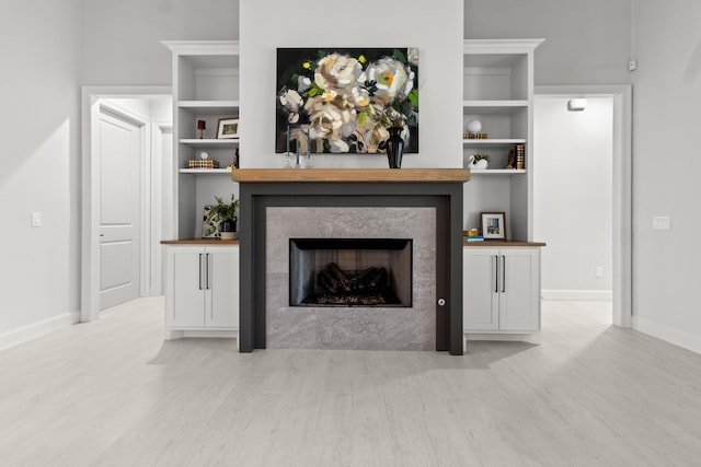 living area with light wood-style floors, a fireplace, baseboards, and built in features