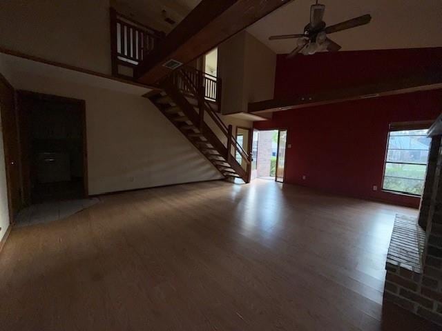 unfurnished living room with stairs, a high ceiling, wood finished floors, and a ceiling fan