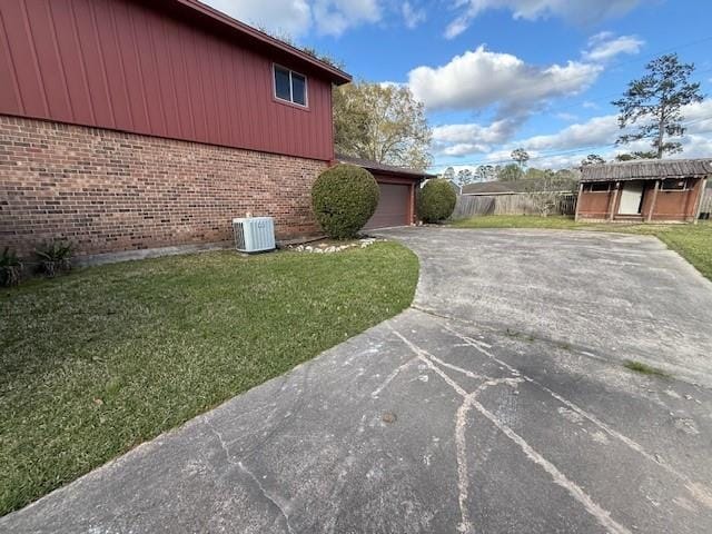 view of property exterior with brick siding, concrete driveway, central AC, and a lawn