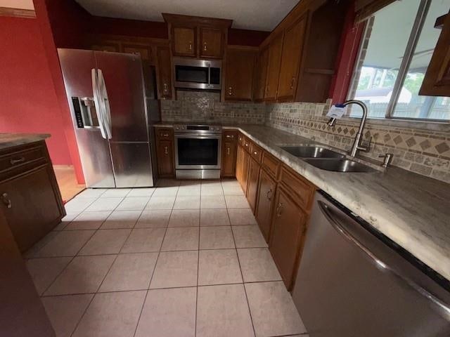 kitchen with backsplash, light tile patterned floors, a sink, and stainless steel appliances