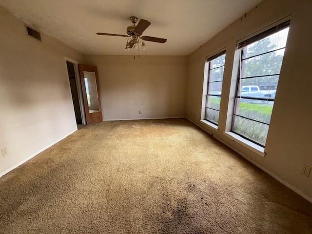 empty room featuring ceiling fan, visible vents, and light carpet