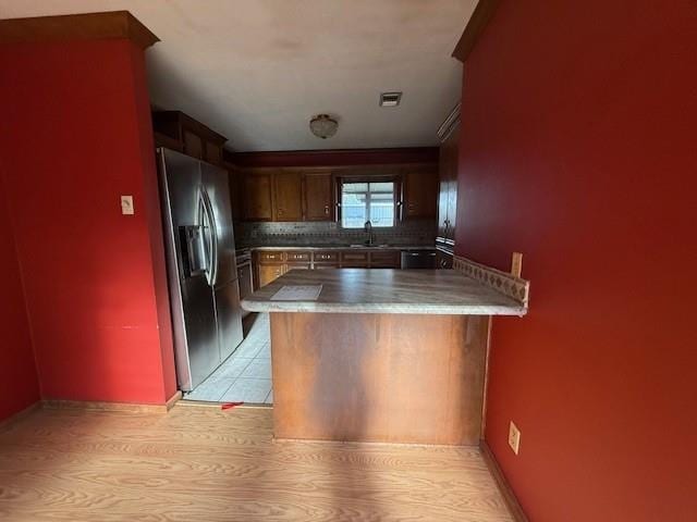 kitchen with backsplash, stainless steel fridge, a peninsula, visible vents, and light wood-style floors