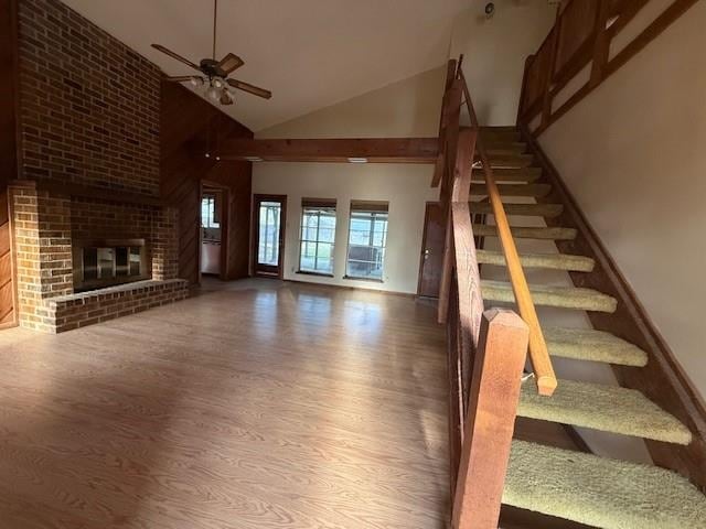 staircase featuring a fireplace, high vaulted ceiling, wood finished floors, and ceiling fan