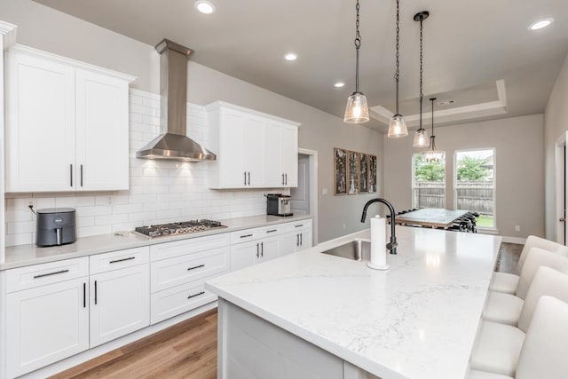 4813 Augusta Dr, Groves, TX 77619 - kitchen with wall chimney exhaust hood, stainless steel gas cooktop, light wood-style flooring, tasteful backsplash, and a kitchen island with sink