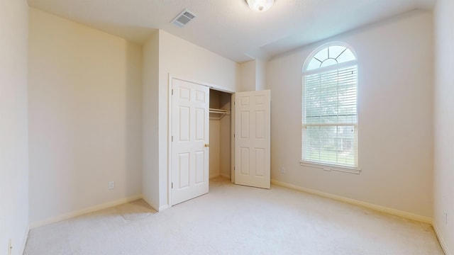 unfurnished bedroom with light carpet, baseboards, visible vents, and a closet