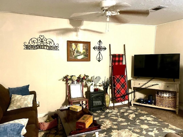 living room featuring carpet, a textured ceiling, a wood stove, and ceiling fan