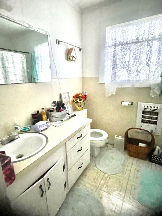 bathroom featuring heating unit, a wealth of natural light, vanity, and toilet