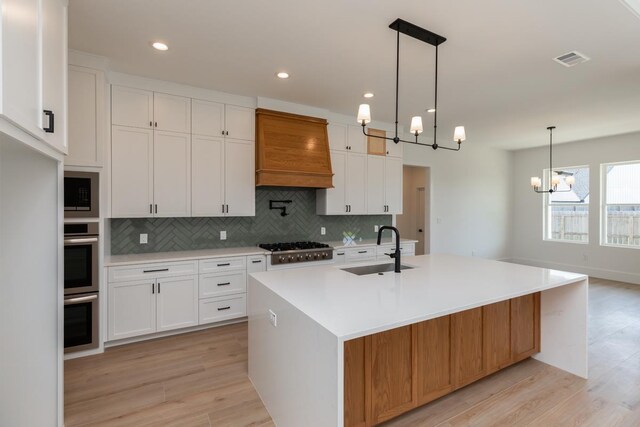 3580 Lily Ln, Beaumont, TX 77713 - kitchen with a sink, custom range hood, appliances with stainless steel finishes, a chandelier, and light wood finished floors