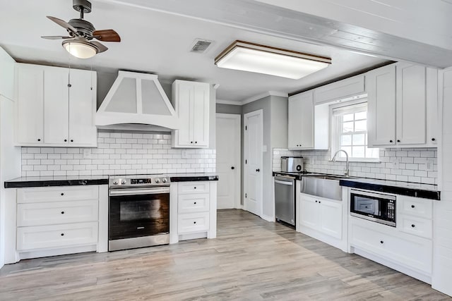 845 Flicker St, Bridge City, TX 77611 - kitchen with stainless steel appliances, custom exhaust hood, dark countertops, ceiling fan, and white cabinetry
