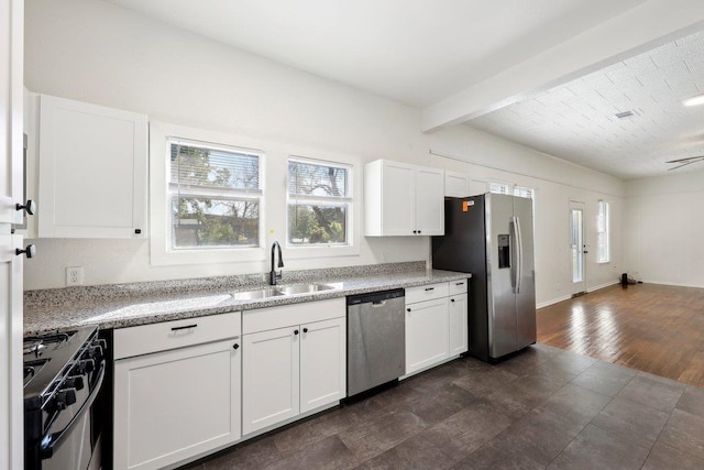 kitchen featuring light stone countertops, white cabinets, a sink, vaulted ceiling with beams, and stainless steel appliances