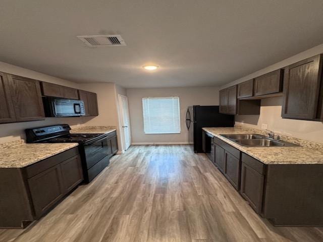 kitchen featuring black appliances, sink, light wood-type flooring, light stone counters, and dark brown cabinetry