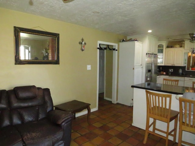 kitchen with a textured ceiling, a peninsula, white cabinets, stainless steel fridge with ice dispenser, and dark countertops