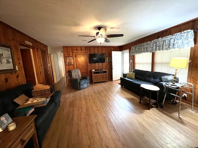 living room with ceiling fan, light hardwood / wood-style floors, and wooden walls