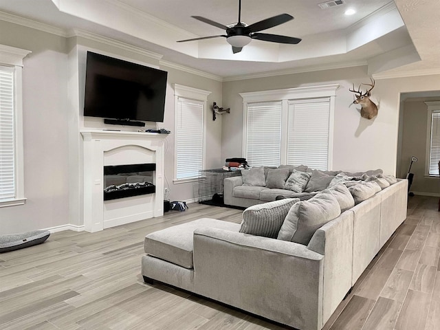 living room with light hardwood / wood-style floors, a raised ceiling, ceiling fan, and crown molding