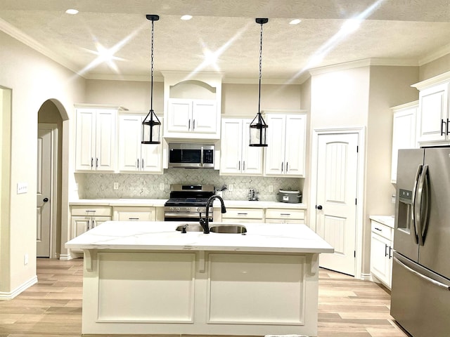 kitchen with light stone countertops, appliances with stainless steel finishes, white cabinetry, hanging light fixtures, and an island with sink