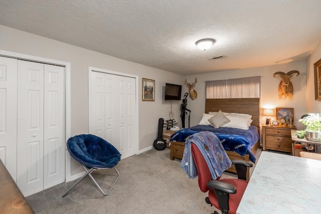 bedroom with multiple closets, light carpet, and a textured ceiling