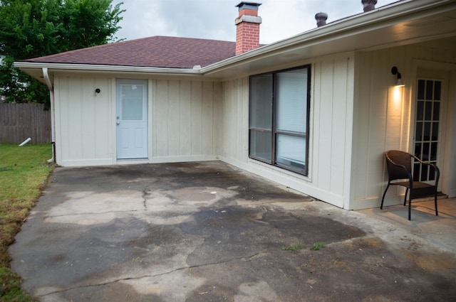exterior space with a shingled roof, fence, a chimney, and a patio area