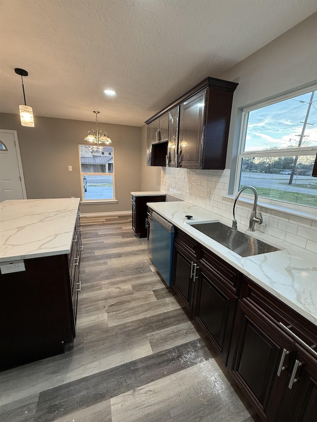 kitchen with light wood finished floors, decorative backsplash, dishwasher, decorative light fixtures, and a sink