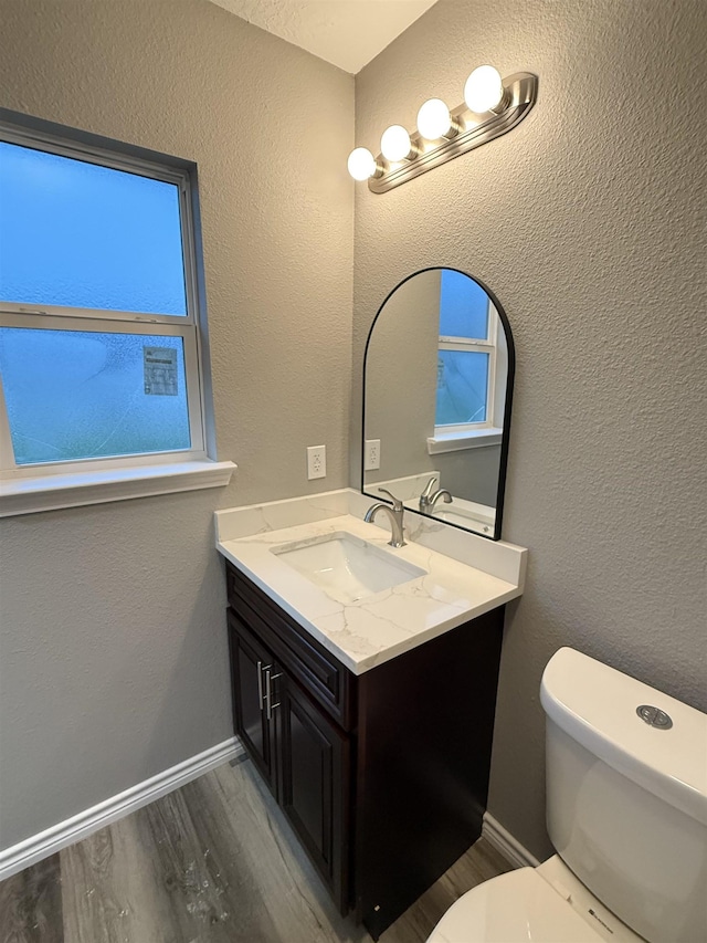 half bathroom with baseboards, a textured wall, toilet, wood finished floors, and vanity