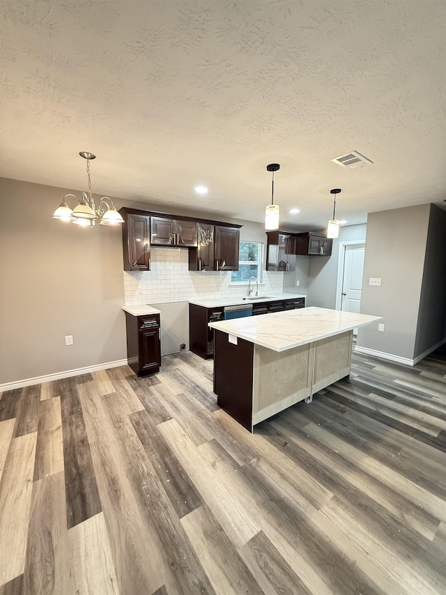 kitchen featuring a kitchen island, backsplash, wood finished floors, dark brown cabinets, and a sink