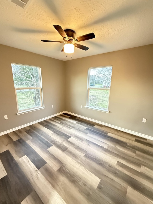 unfurnished room featuring a healthy amount of sunlight, a textured ceiling, baseboards, and wood finished floors