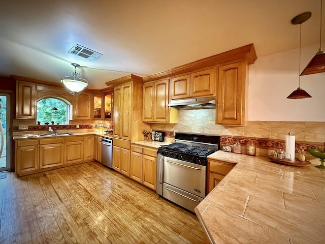 2940 36th St, Port Arthur, TX 77642 - kitchen featuring stainless steel appliances, under cabinet range hood, light countertops, hanging light fixtures, and tasteful backsplash