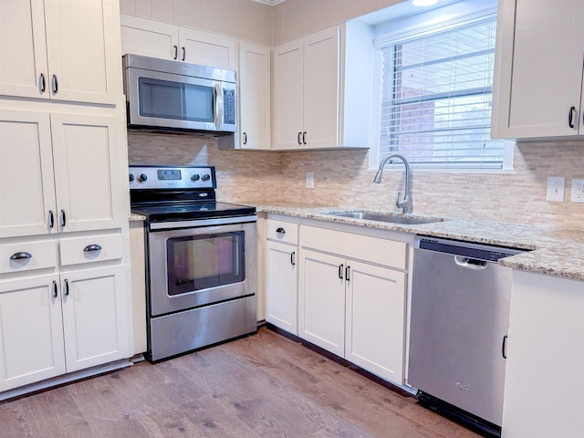 kitchen with appliances with stainless steel finishes, light wood-type flooring, light stone counters, sink, and white cabinets