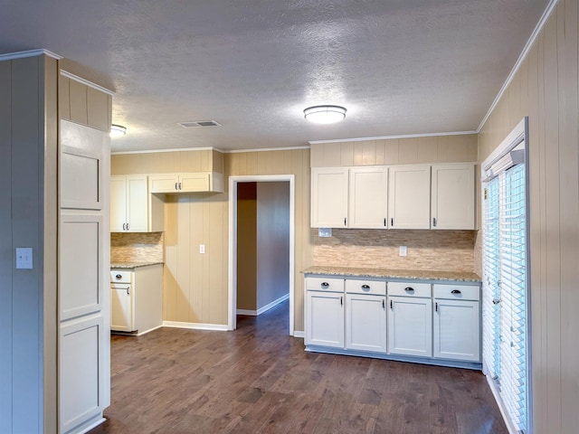 kitchen with dark wood-type flooring, white cabinetry, ornamental molding, and light stone counters