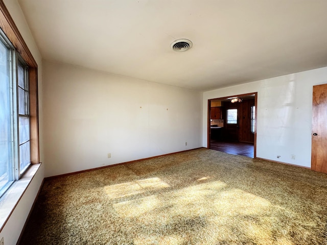 spare room featuring dark colored carpet, visible vents, and baseboards