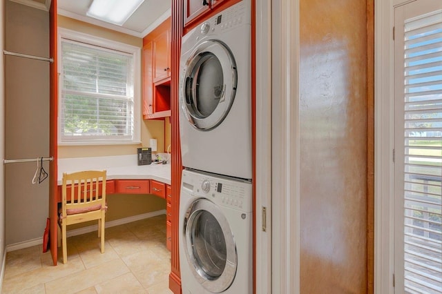 laundry area with cabinets, light tile patterned floors, crown molding, and stacked washer and clothes dryer