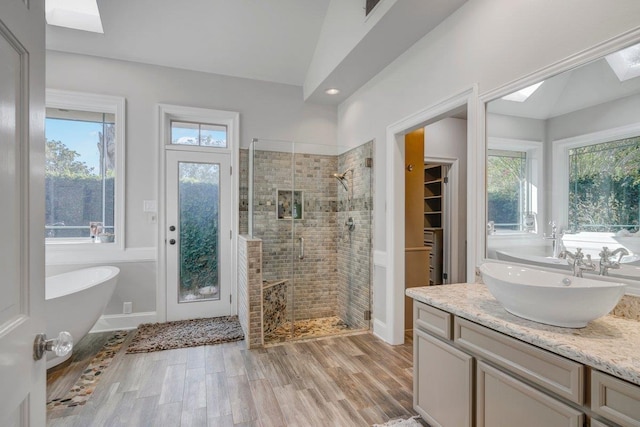 bathroom featuring a wealth of natural light, vaulted ceiling with skylight, plus walk in shower, and wood-type flooring