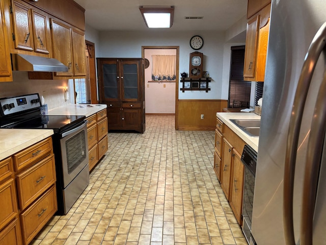 kitchen featuring ventilation hood, sink, stainless steel appliances, and wooden walls