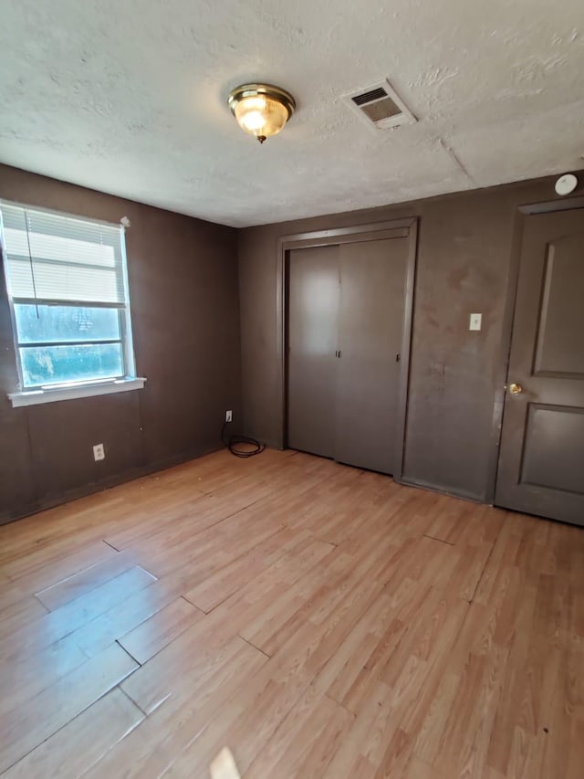 unfurnished bedroom featuring a closet, light hardwood / wood-style floors, and a textured ceiling