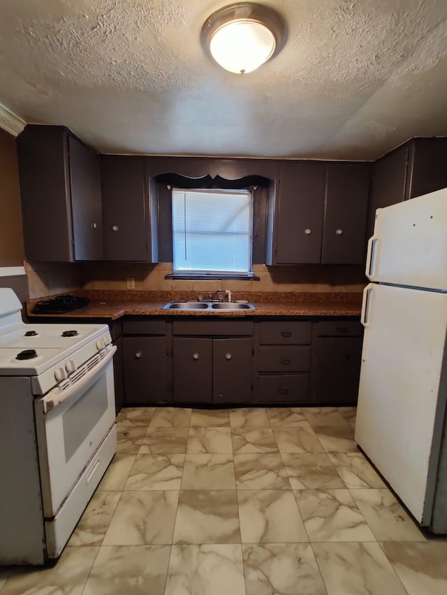 kitchen with a textured ceiling, dark brown cabinets, sink, and white appliances