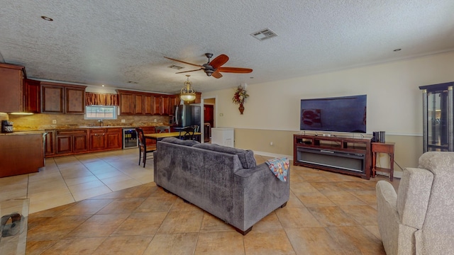 living room featuring a textured ceiling, ceiling fan, sink, wine cooler, and light tile patterned flooring