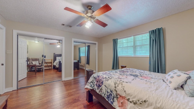 bedroom with hardwood / wood-style floors, a textured ceiling, ceiling fan, and multiple closets