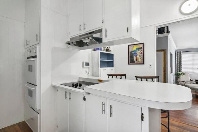 kitchen with a kitchen bar, kitchen peninsula, white cabinetry, and double oven