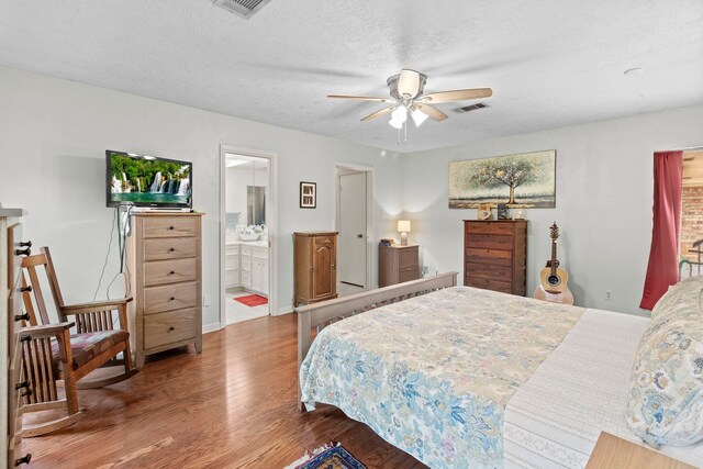 bedroom with a textured ceiling, wood finished floors, visible vents, and connected bathroom