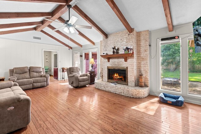 living room featuring lofted ceiling with beams, visible vents, a ceiling fan, hardwood / wood-style flooring, and a stone fireplace