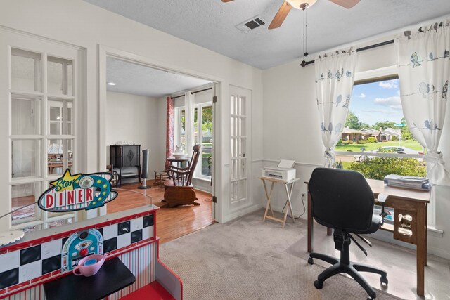carpeted office with a textured ceiling, visible vents, ceiling fan, and french doors