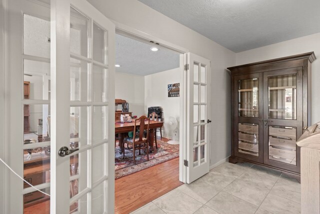 doorway to outside featuring baseboards, french doors, a textured ceiling, and light tile patterned floors