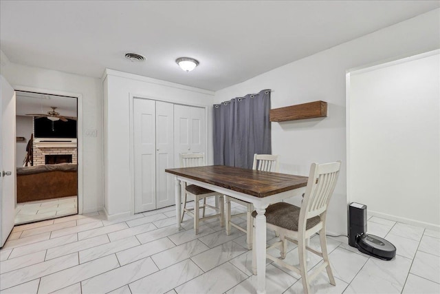 dining room with a brick fireplace, a ceiling fan, visible vents, and baseboards