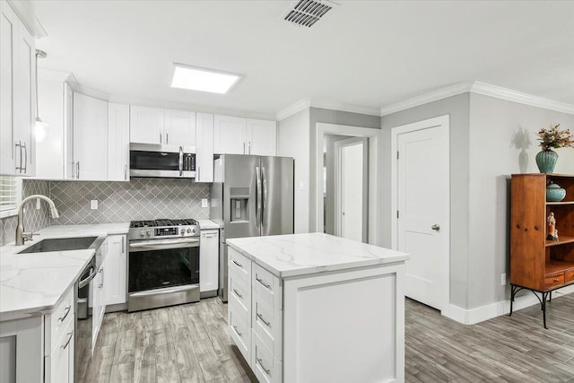 kitchen with appliances with stainless steel finishes, white cabinetry, a kitchen island, and sink