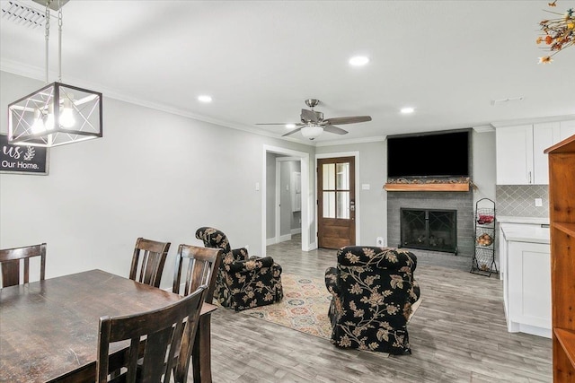 dining room with a fireplace, light hardwood / wood-style flooring, ceiling fan, and crown molding