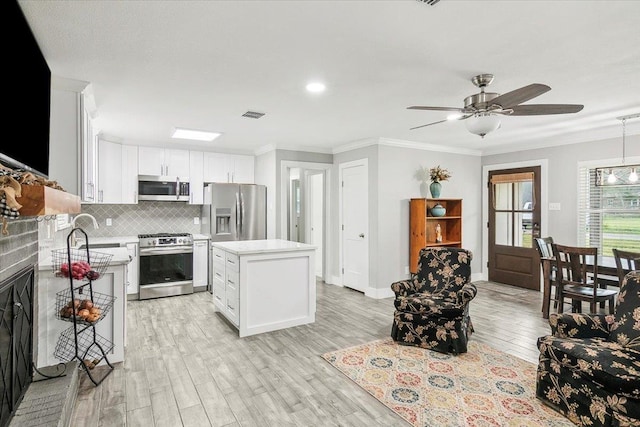 kitchen with light wood-type flooring, appliances with stainless steel finishes, tasteful backsplash, a kitchen island, and white cabinetry