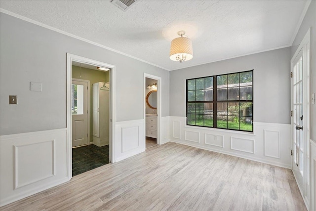 100 Teakwood St, Silsbee, TX 77656 - unfurnished room featuring a wainscoted wall, a textured ceiling, light wood finished floors, a decorative wall, and ornamental molding