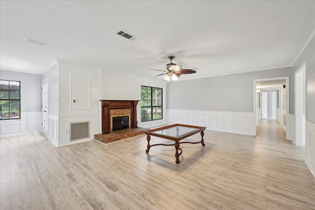 100 Teakwood St, Silsbee, TX 77656 - unfurnished living room featuring a decorative wall, a textured ceiling, light wood-type flooring, a brick fireplace, and a ceiling fan