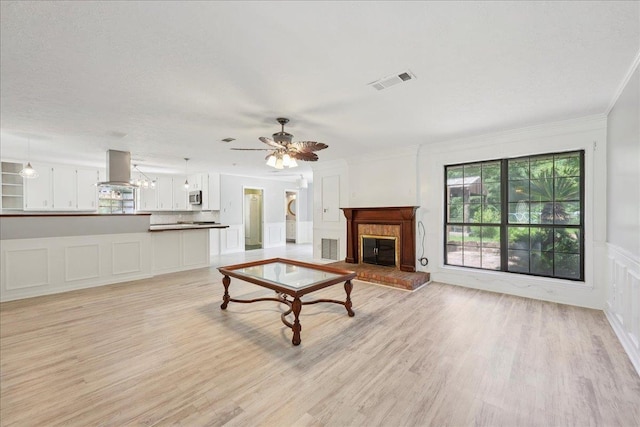 100 Teakwood St, Silsbee, TX 77656 - unfurnished living room with a decorative wall, light wood-style flooring, a fireplace, ornamental molding, and ceiling fan