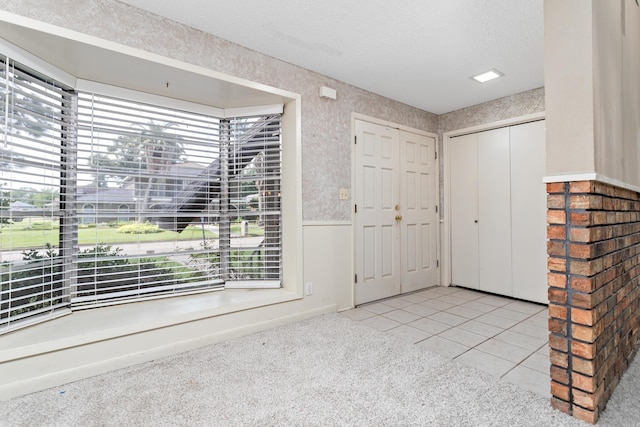 carpeted foyer featuring tile patterned flooring, wainscoting, a textured ceiling, and wallpapered walls